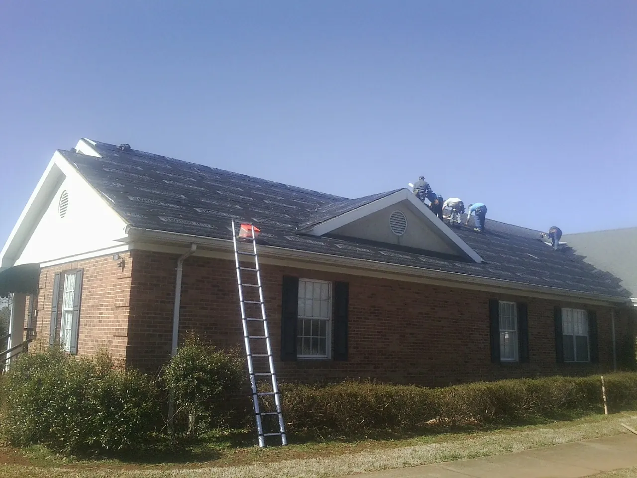 Crew tearing shingles off a brick ranch roof with a ladder set — Metal Roof Repair work by our crew in Rockville