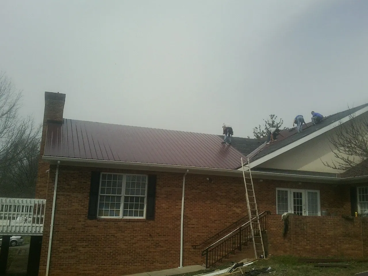 Crew setting red metal roofing panels on a brick home in Rockville